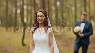 在新鲜空气中的森林里快乐的一对。 新郎带着一束美丽的花向新娘走去。 新娘一动不动地站着